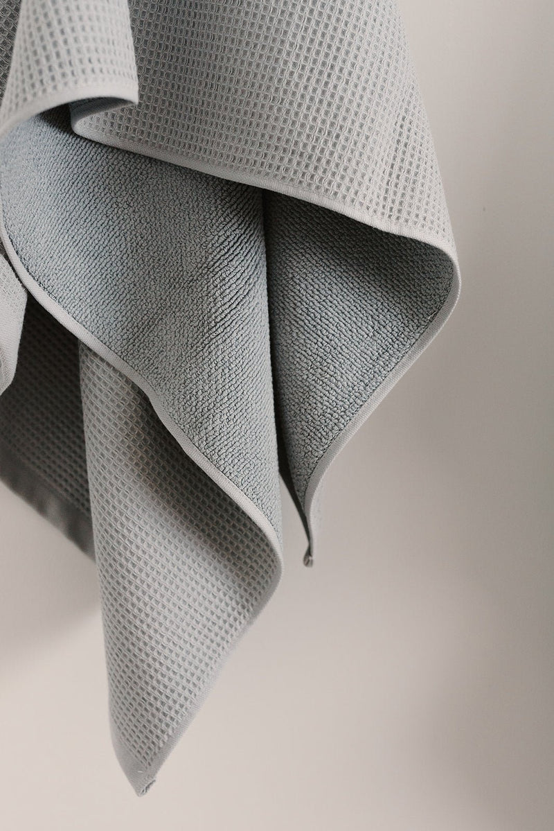 Waffle Bath Towel in the color Harbor Mist. Photo of Harbor Mist Waffle Bath Towel taken hanging from a towel hook in a white bathroom.