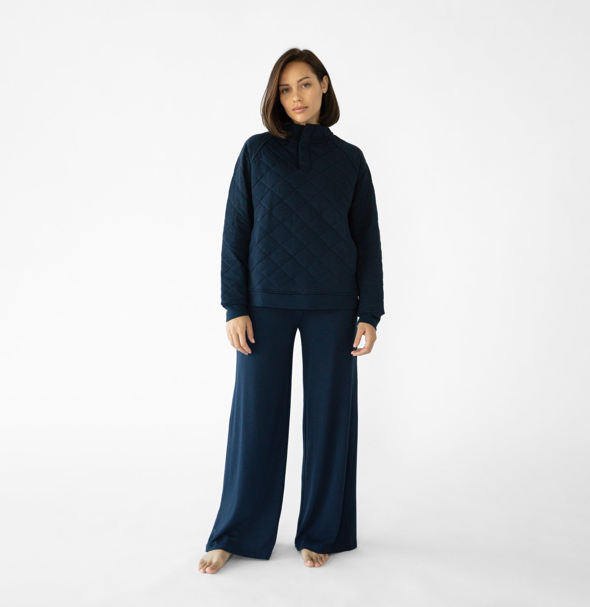 A woman stands in a relaxed pose wearing a navy loungewear set from Cozy Earth, featuring the Women's Ultra-Soft Bamboo Wide Leg Pull On Pant TALL and a matching hooded sweatshirt.  