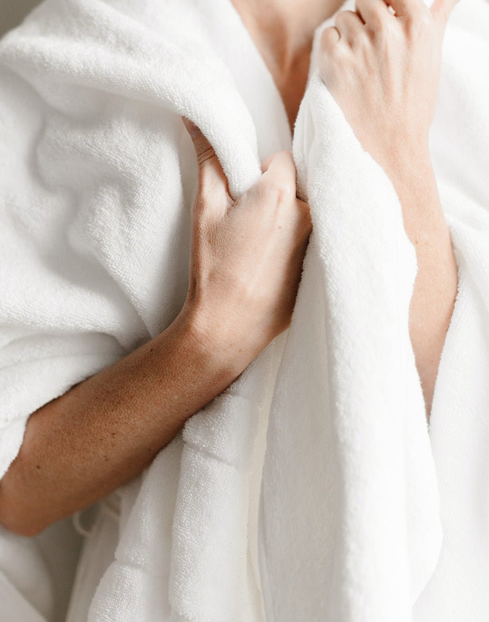 Premium Plush Bath Sheet in the color White. Photo of White Premium Plush Bath Sheet taken with women wrapped in the premium plush bath sheet. The photo is shot from the neck to the torso. 