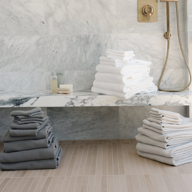Complete Waffle Bath Bundle in the colors Charcoal, White, and Light Grey. Photo of Charcoal, White, and Light Grey Complete Waffle Bath Bundle taken while towels rest on bathroom floor