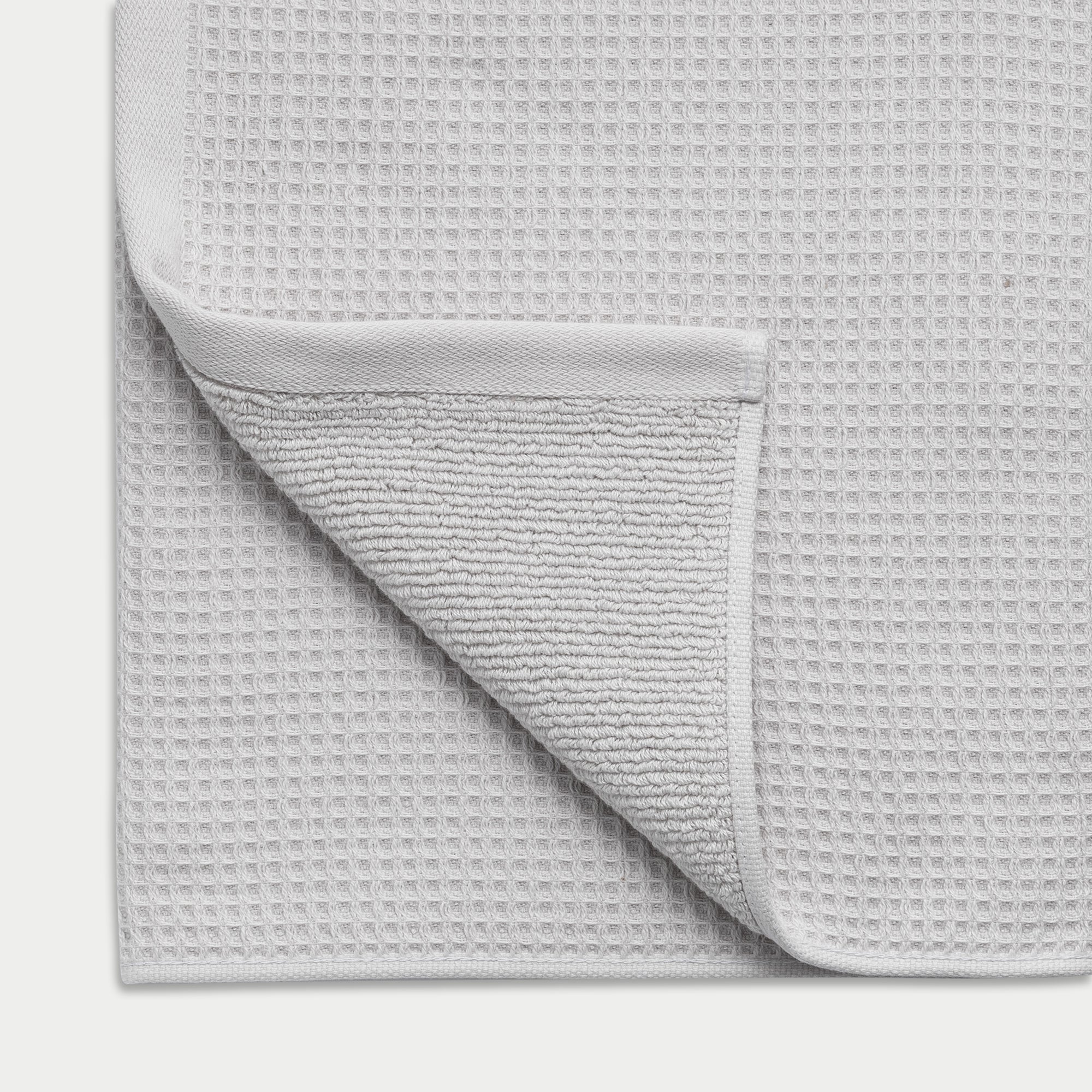 Waffle Bath Towel in the color light grey. Photo of White Waffle Bath Towel taken as a close up of the Waffle Bath Towel. The picture shows the corner of the towel and a white background 
